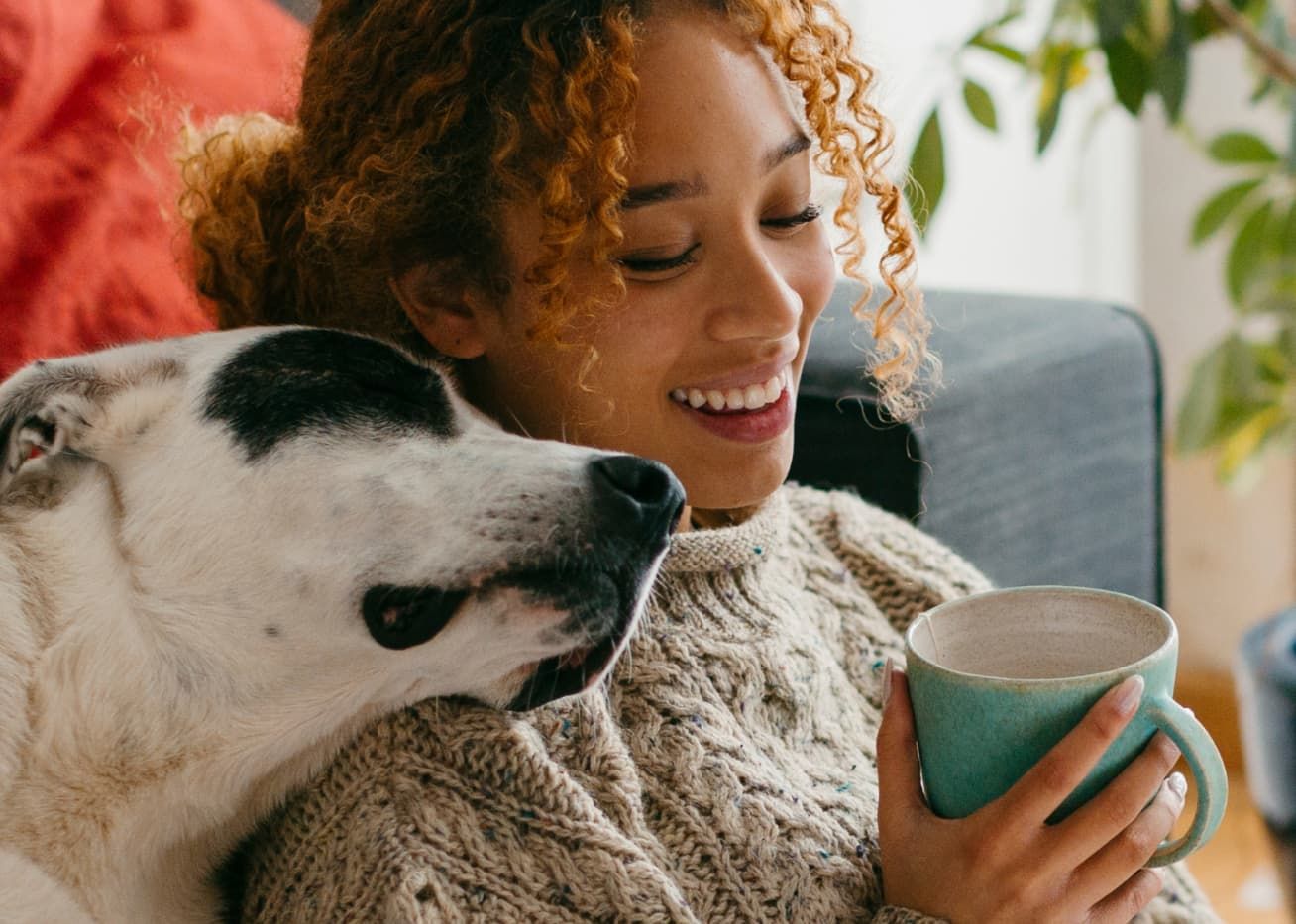 a woman sipping a cup of coffee and his fellow dog close to her